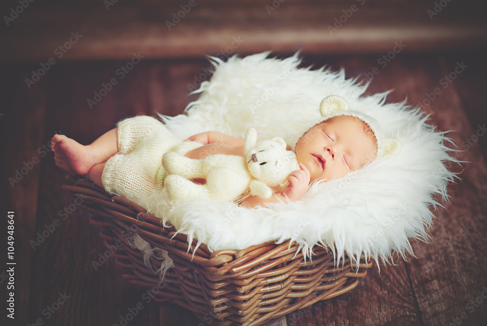 戴着熊帽的可爱新生儿和玩具泰迪熊睡在篮子里