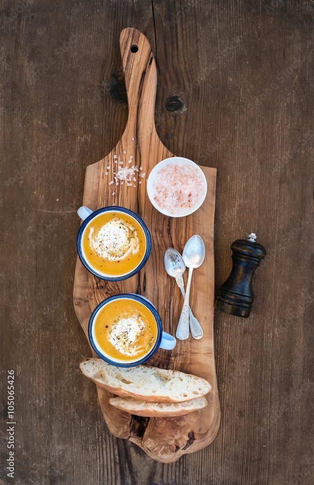 自制南瓜奶油汤，装在搪瓷马克杯里，配香草和新鲜面包片，放在橄榄色的服务板上