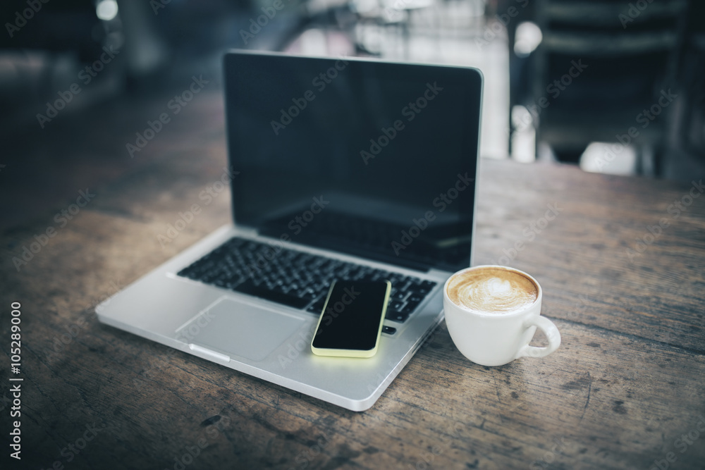 笔记本电脑上的空白手机和木桌上的咖啡杯