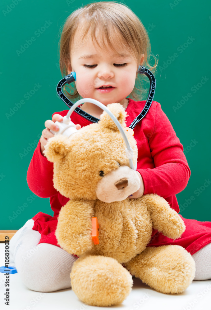 Toddler girl caring for her teddy bear with a stethoscope