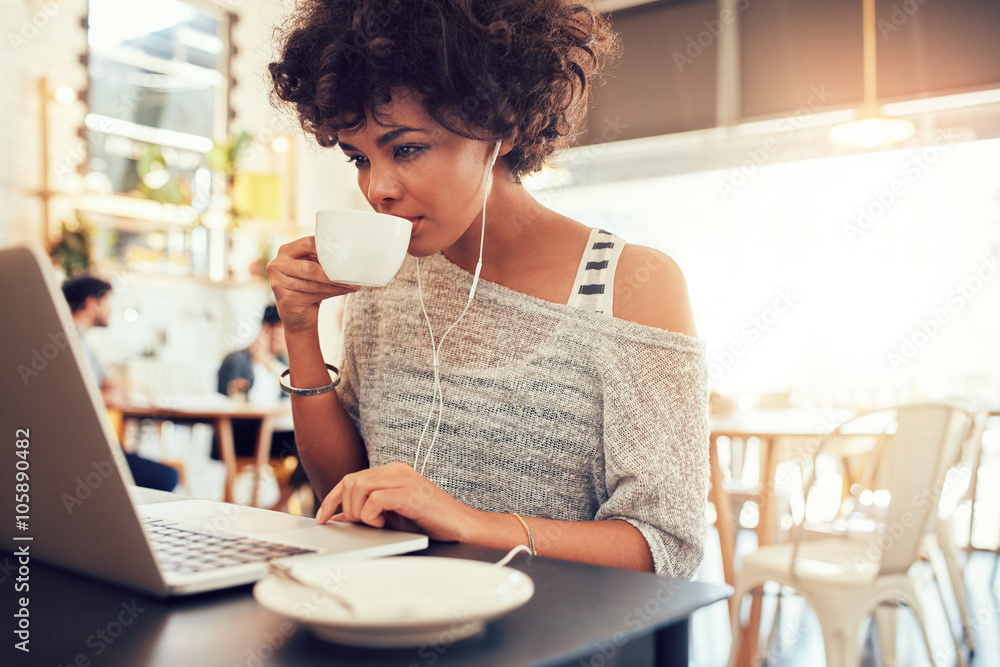 年轻的非洲妇女在咖啡馆喝咖啡并使用笔记本电脑