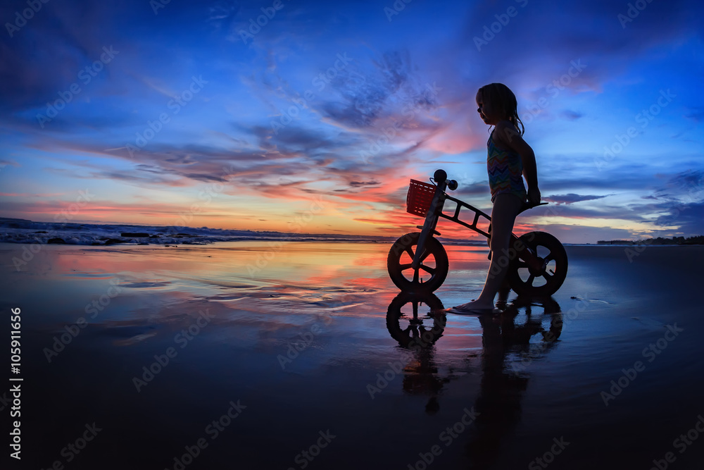 骑自行车的小孩的黑色剪影站在潮湿的沙滩上，看着海浪和科罗拉多