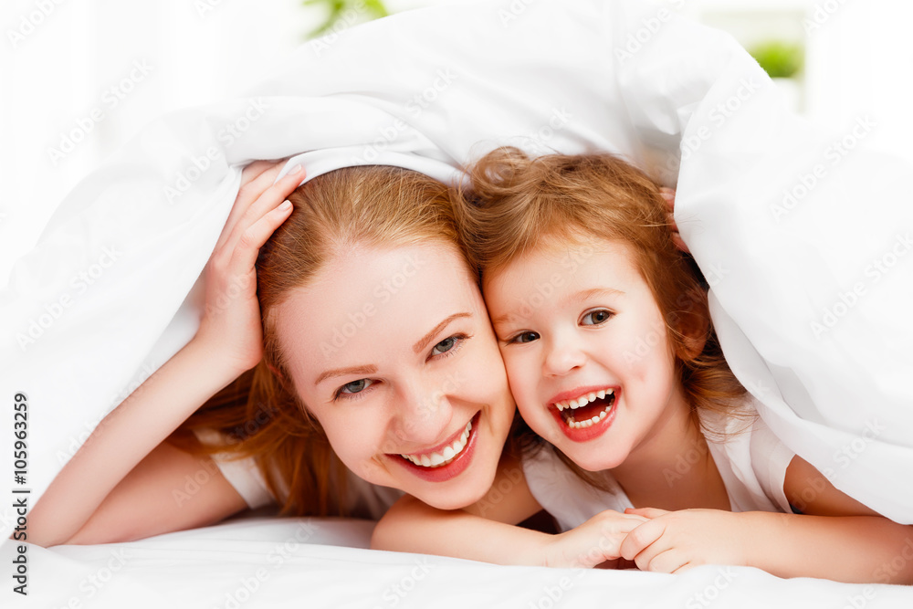 happy family mother and child playing and laughing in bed