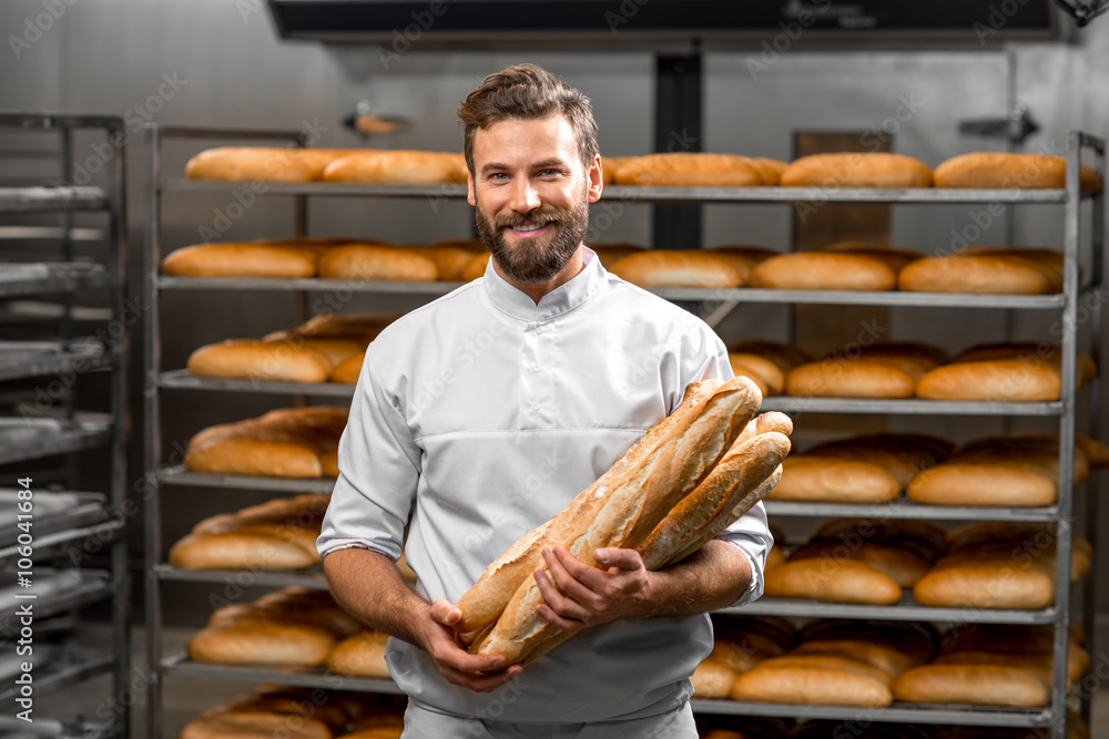 英俊的面包师穿着制服，手里拿着法棍，背景是面包架