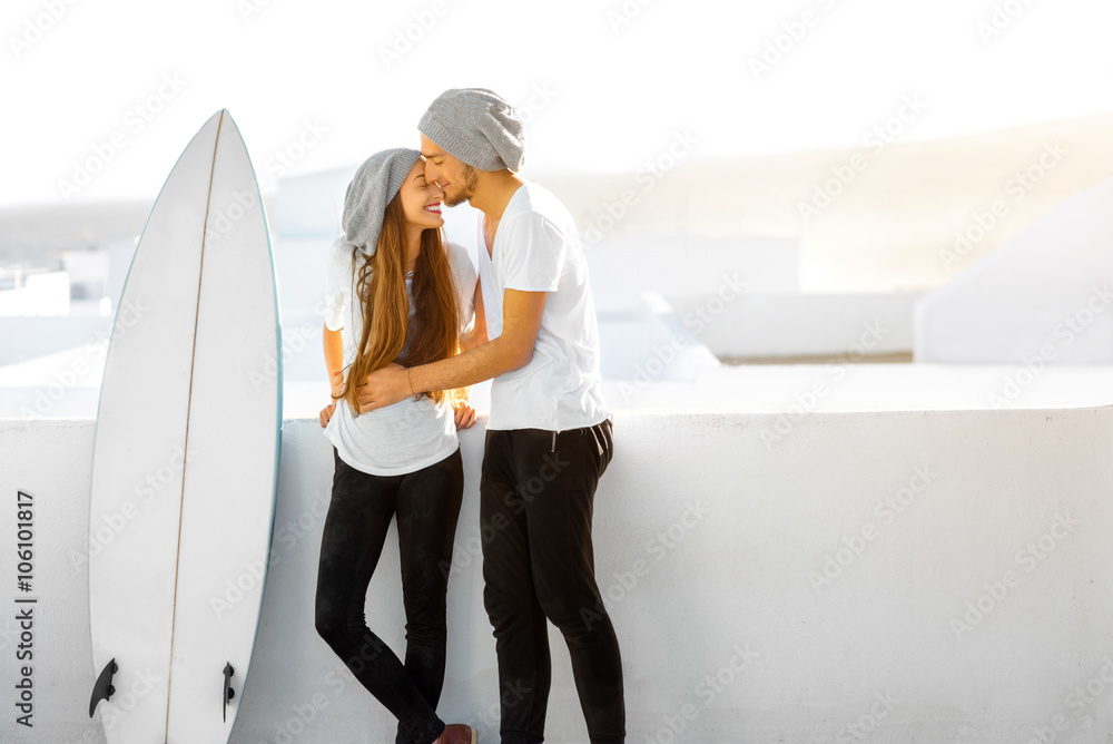 一对年轻夫妇穿着白色t恤，戴着帽子，带着冲浪板享受暑假