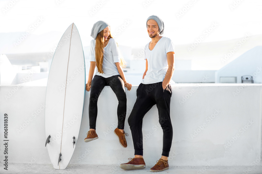 一对年轻夫妇穿着白色t恤，戴着帽子，带着冲浪板享受暑假