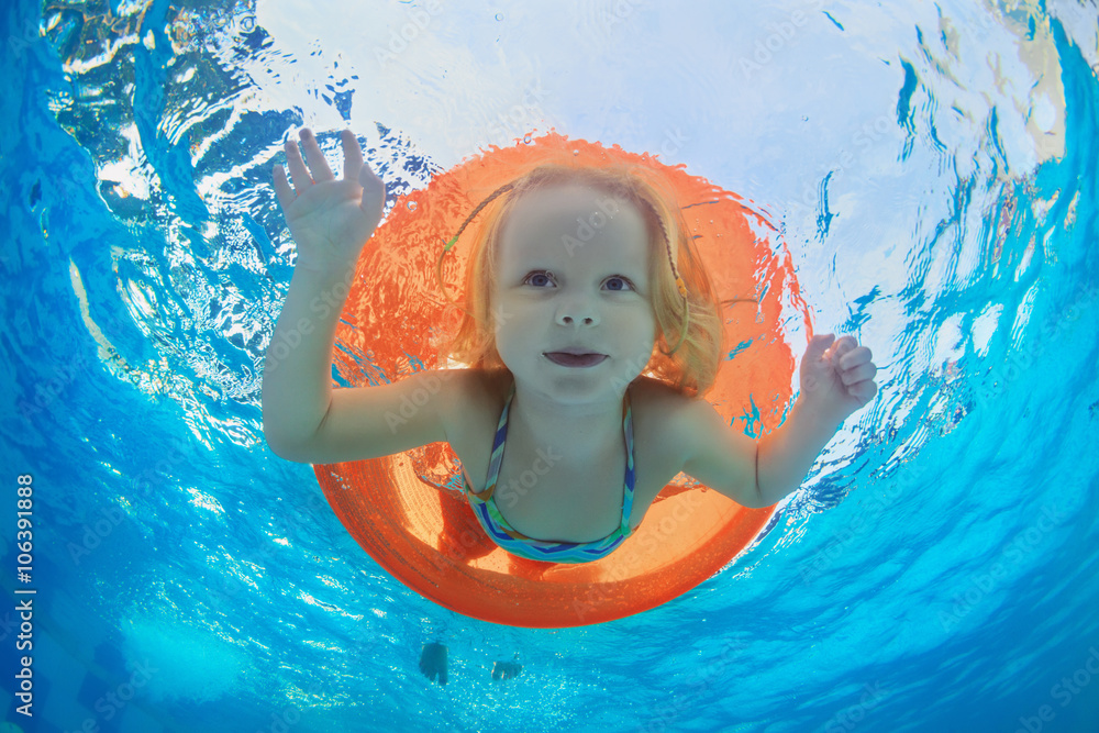 一张有趣的水下照片，照片中的女婴在橙色的管子上有趣地游泳，并在清澈的水上公园潜水p