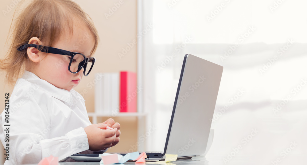 聪明的蹒跚学步的女孩戴着大眼镜用笔记本电脑
