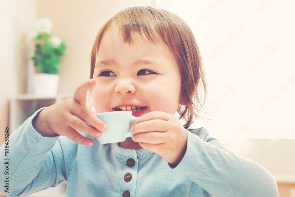 快乐的蹒跚学步的女孩用茶杯喝水