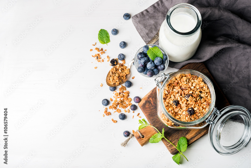 健康早餐食材。打开玻璃罐的自制格兰诺拉麦片、牛奶或酸奶瓶、蓝莓