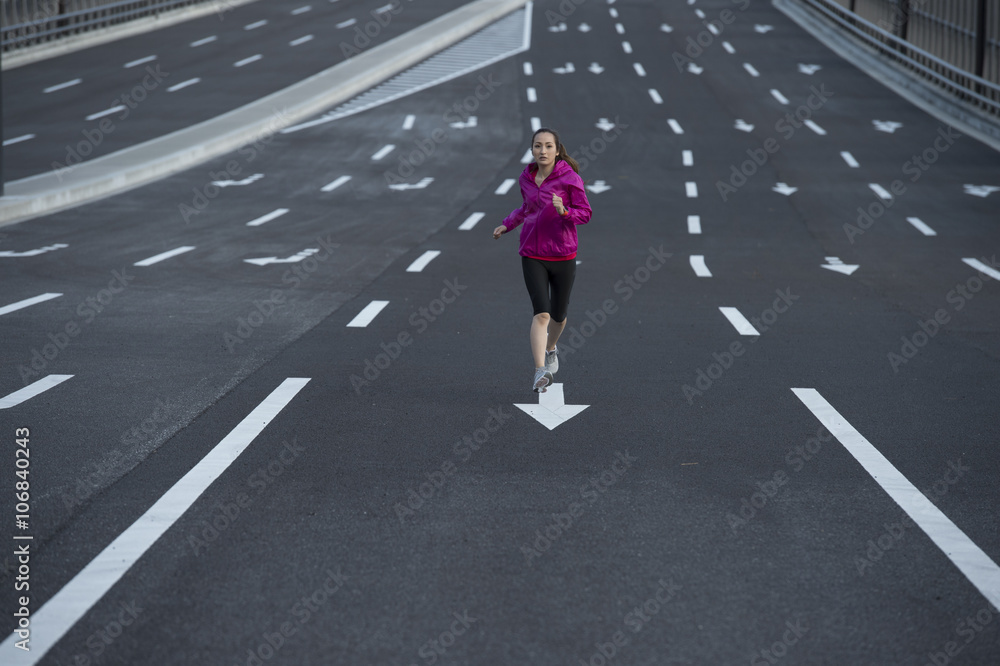 女人穿着运动服在宽阔的马路中间跑步