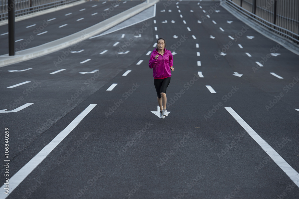 女人穿着运动服在宽阔的马路中间跑步