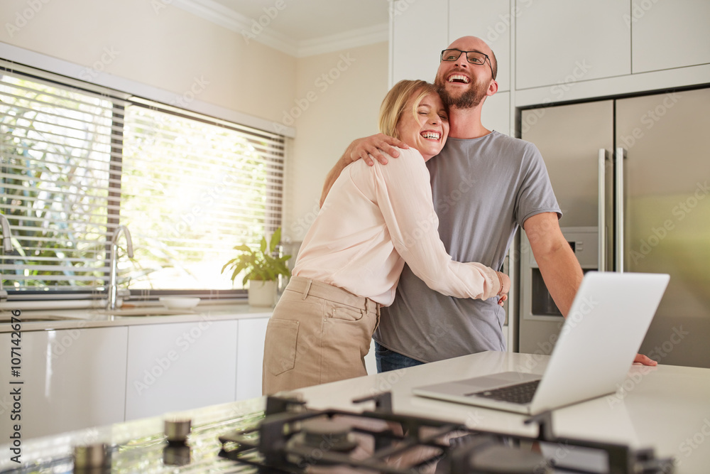 Loving couple with laptop in kitchen at home