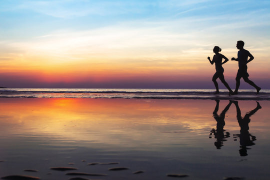 海滩上的两名跑步者，日落时慢跑的人的剪影，健康的生活方式背景