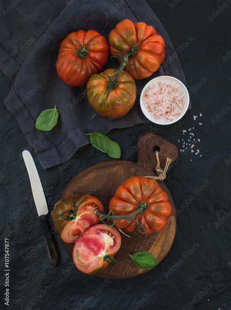 在黑色石头背景下的乡村木板上，新鲜成熟的发际番茄和罗勒叶。
