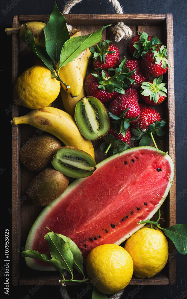 深色背景下木托盘中各种五颜六色的热带水果