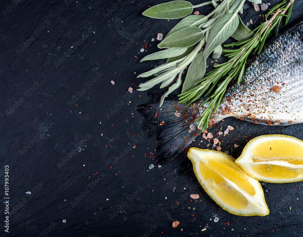 新鲜生多拉多鱼或鲷鱼的尾巴放在黑石板石板上，配香料、香草、柠檬和