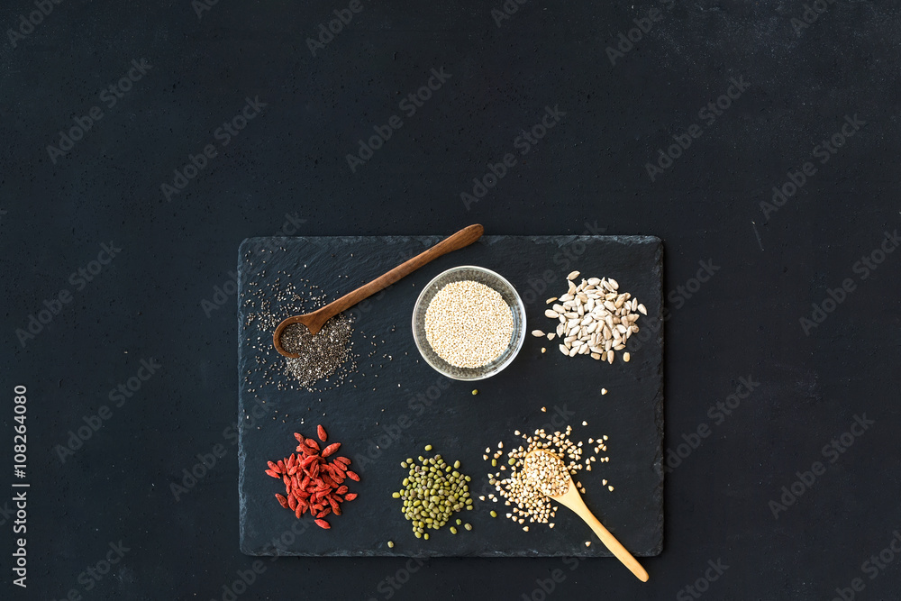 Superfoods on black chalkboard background: goji berries, chia, mung beans, buckwheat, quinoa, sunflo