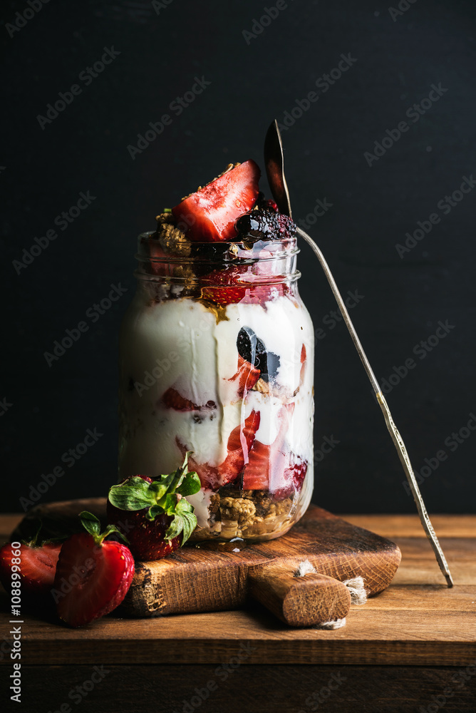 酸奶燕麦格兰诺拉麦片配草莓、桑椹、蜂蜜和薄荷叶，装在黑色b的高玻璃罐中