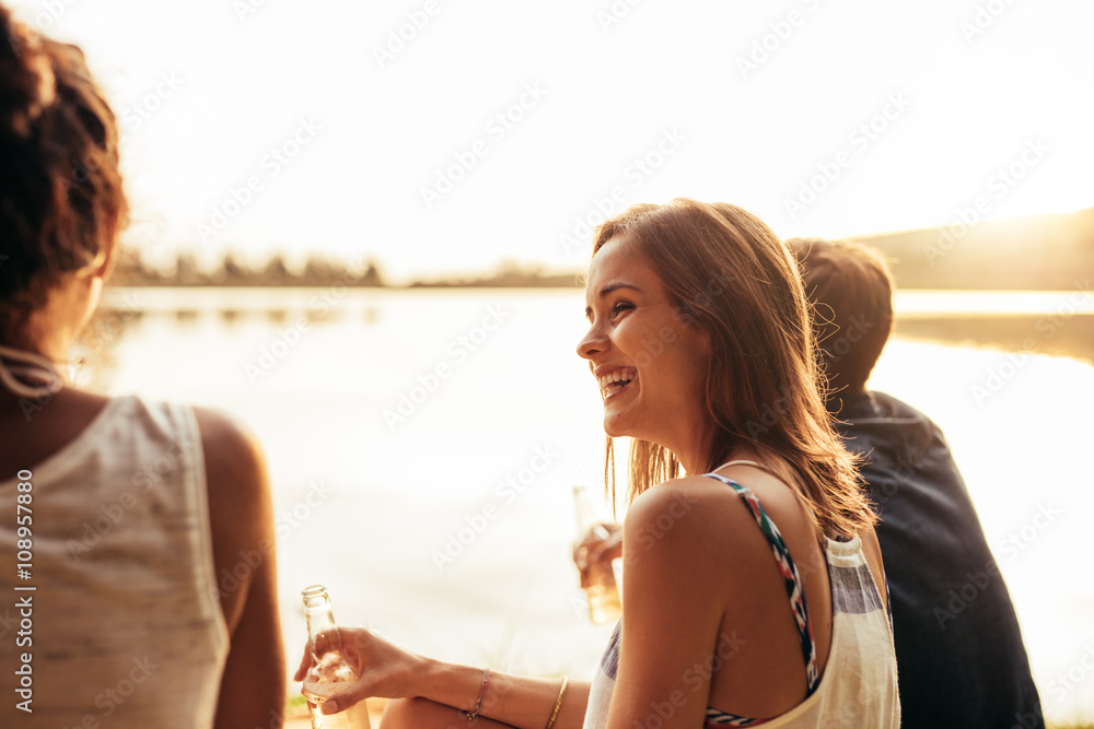 微笑的年轻女孩和朋友坐在湖边