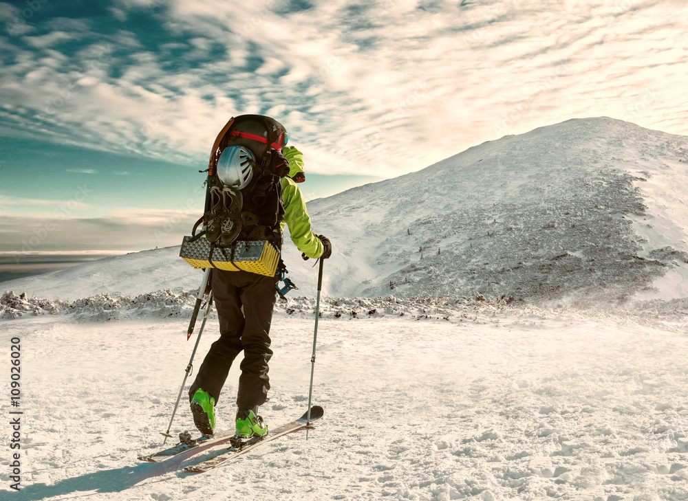 滑雪时背着背包的男人在阳光下登上山顶