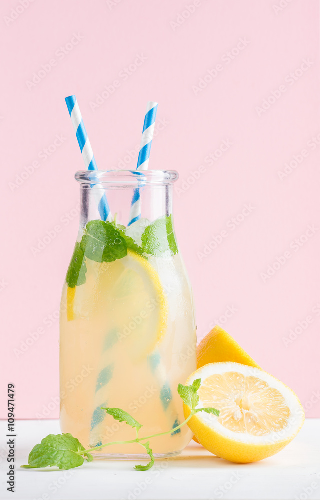 一瓶自制柠檬水，配薄荷、冰、柠檬、纸吸管和淡粉色背景