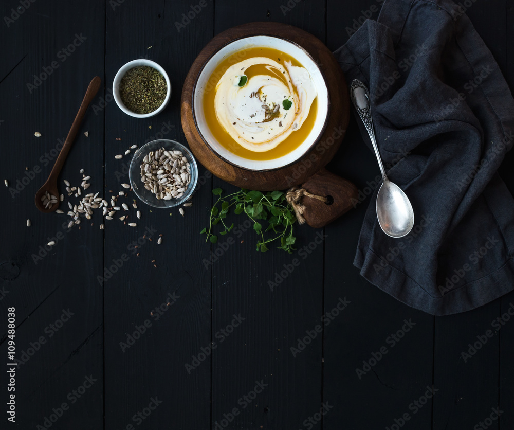 南瓜汤，奶油、种子和香料，装在乡村金属碗中，黑色背景。俯视图。