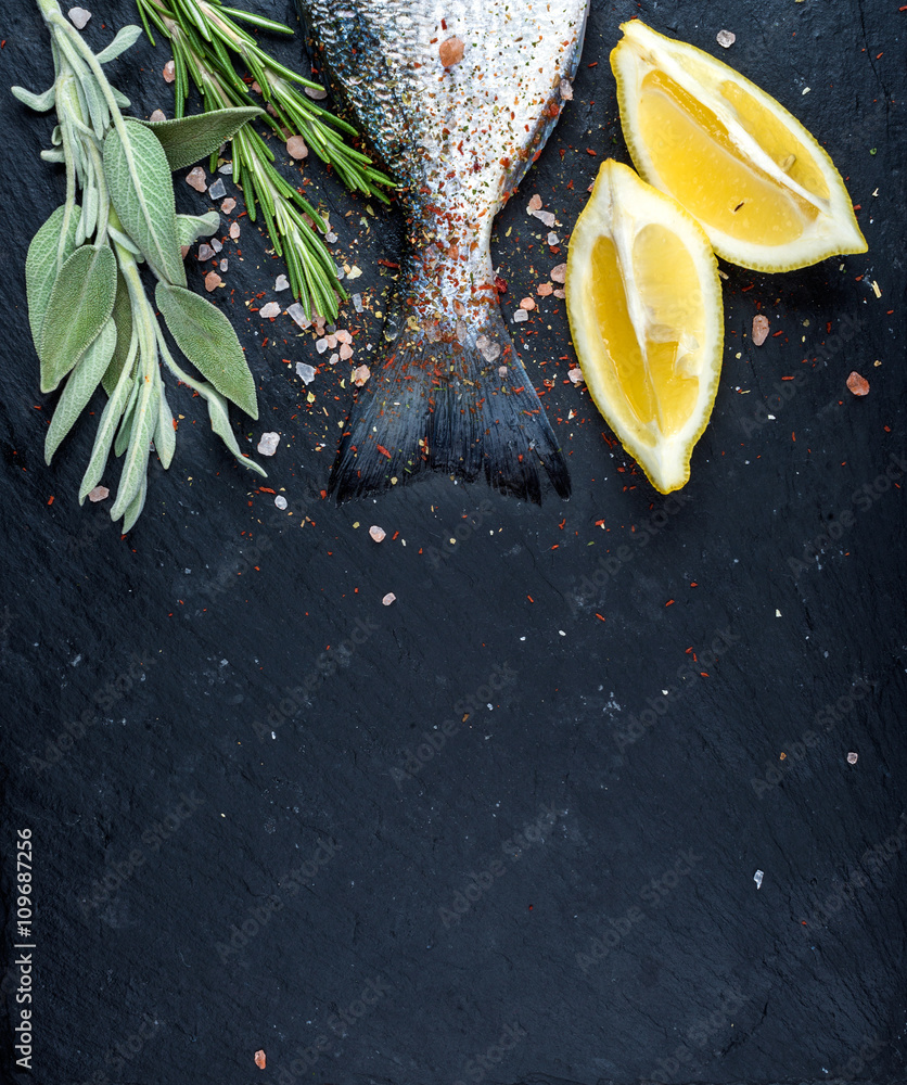 新鲜生多拉多鱼或鲷鱼的尾巴放在黑石板石板上，配香料、香草、柠檬和