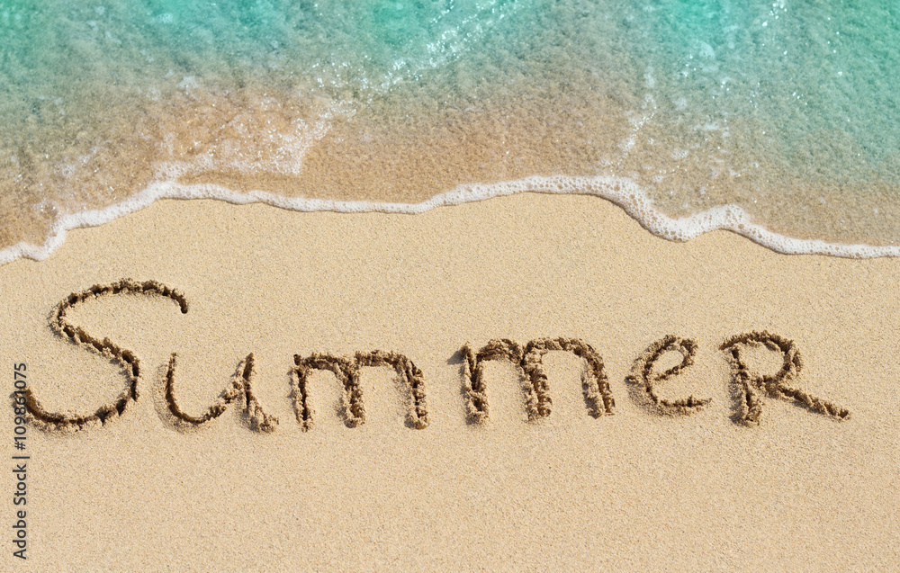 在沙子上手写的单词Summer，背景是短暂的海浪