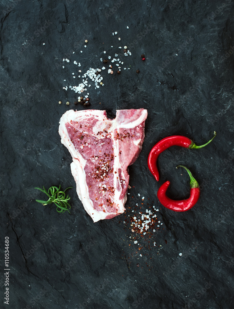 Raw fresh meat t-bone steak with spices, chili peppers and rosemary over black slate stone backgroun
