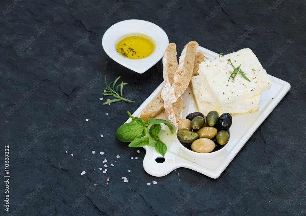 新鲜的羊乳酪配橄榄、罗勒、迷迭香和面包片，放在白色陶瓷服务板上