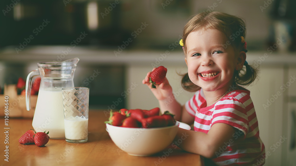 快乐的小女孩在夏天的家庭厨房吃草莓