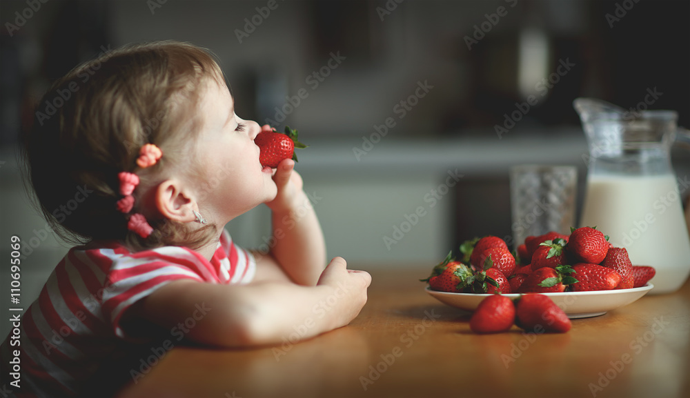 快乐的小女孩在夏天的家庭厨房里吃草莓