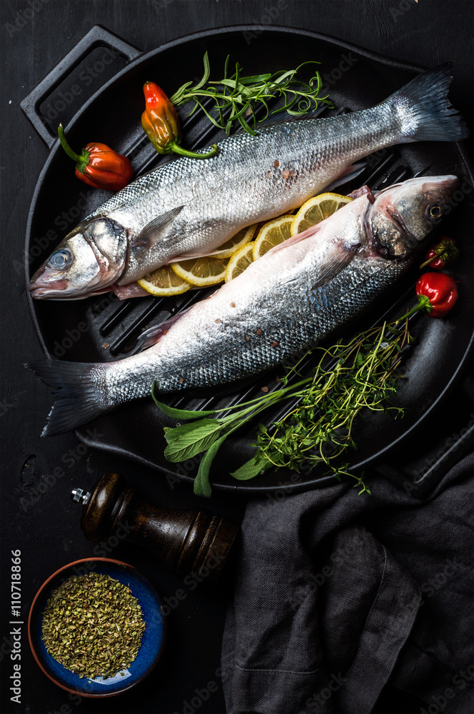 生生未煮熟的鲈鱼，配香草和香料，放在黑色木质背景的铸铁烹饪锅中