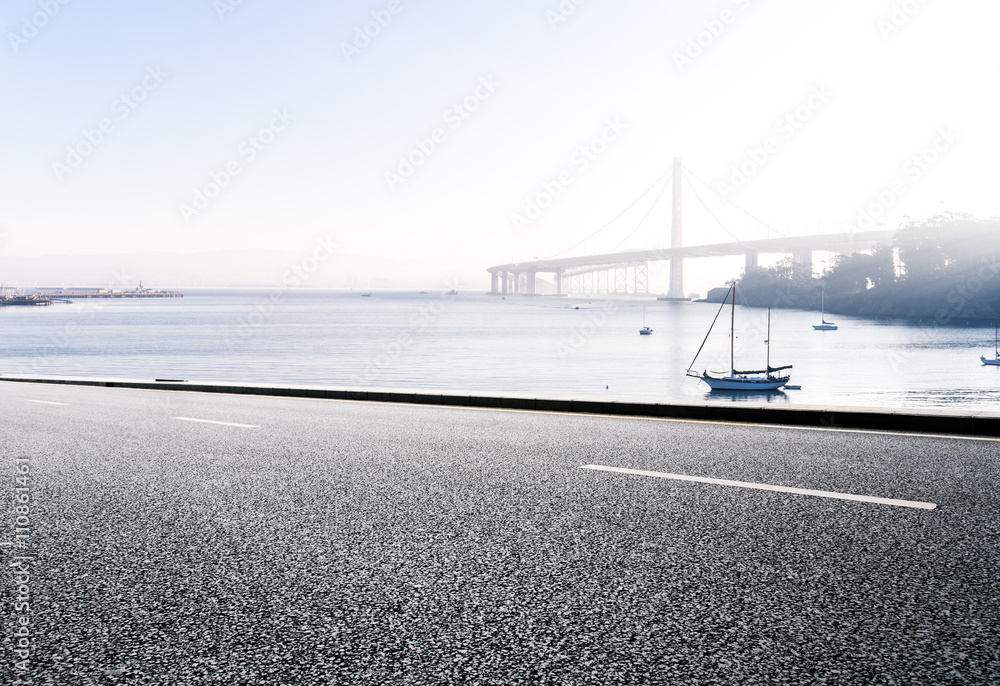 empty asphalt road with sail boat on tranquil water and distant