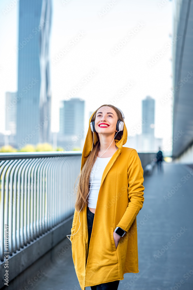 穿着黄色毛衣的年轻女性音乐爱好者在现代桥上用天窗听音乐