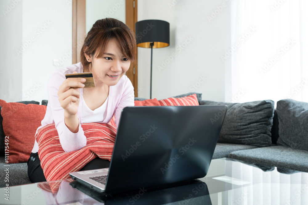 亚洲年轻女子坐在沙发上在家上网购物