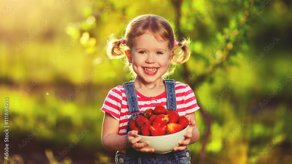 happy laughing child girl with ripe strawberry in summer on natu