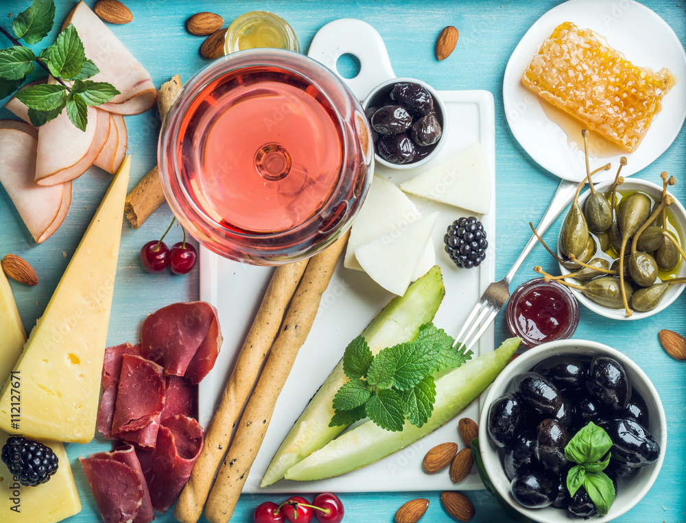 Summer wine snack set. Glass of rose, meat, cheese, olives, honey, bread sticks, nuts, capers and be