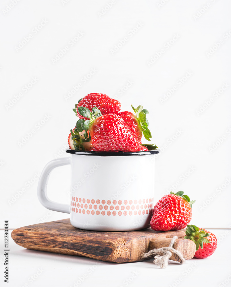 新鲜成熟的红色草莓，装在乡村风格的搪瓷马克杯上，装在白色背景的乡村木板上