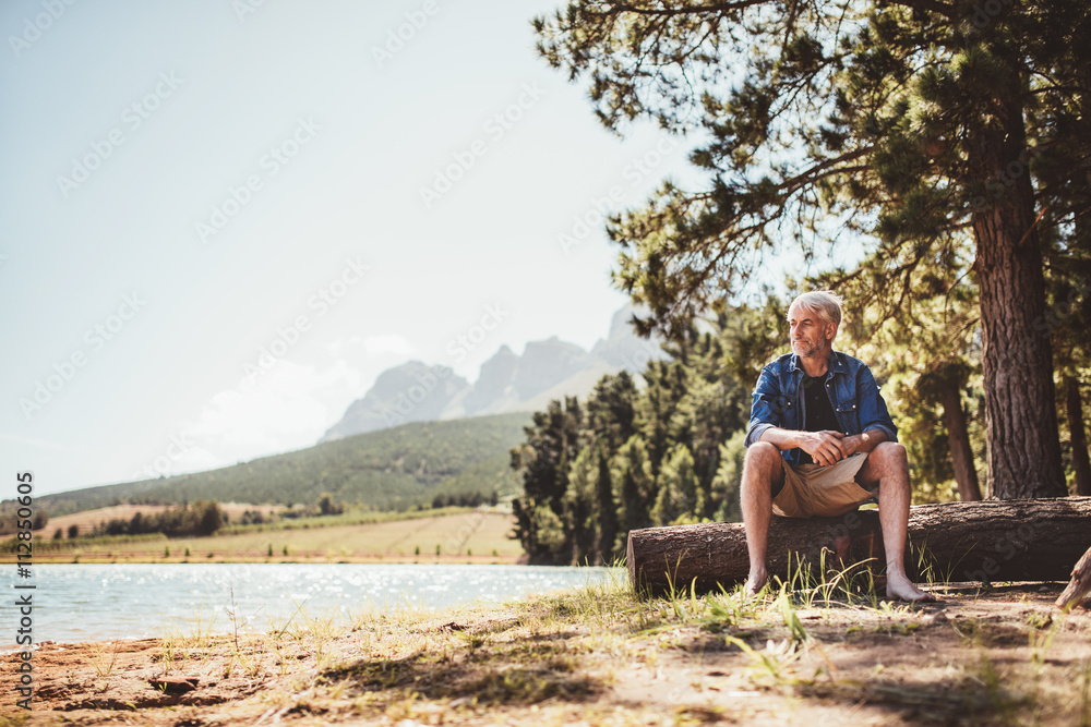 成熟的男人坐在湖边的木头上