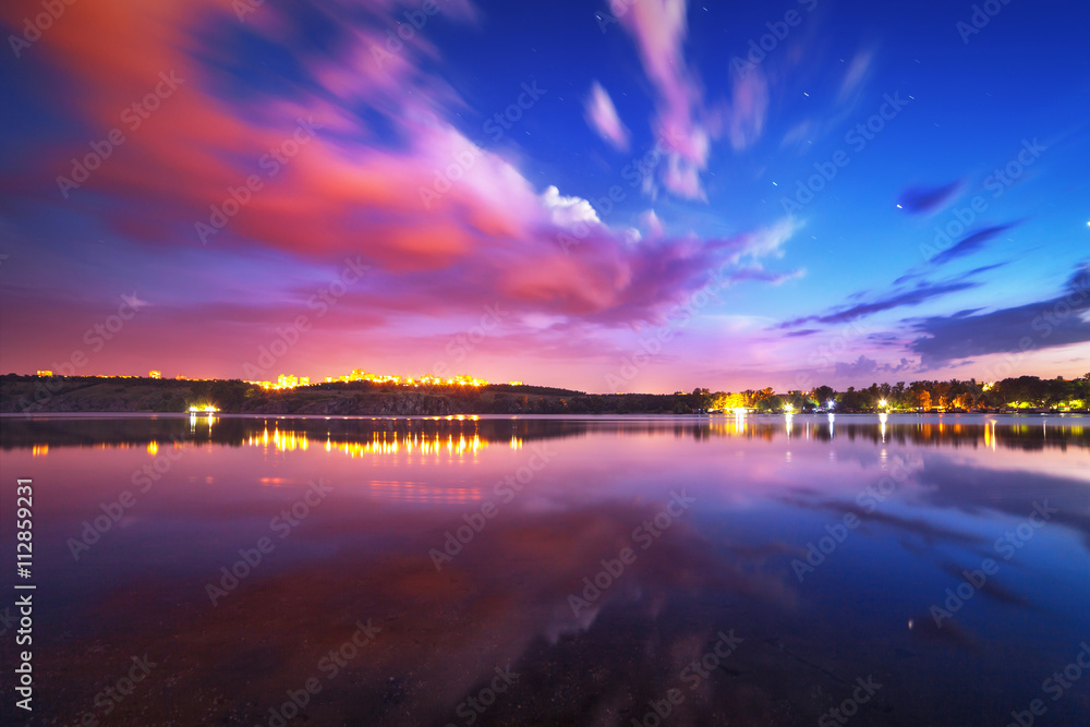 Colorful night landscape on the lake with blue sky and moving clouds reflected in water. Nature back
