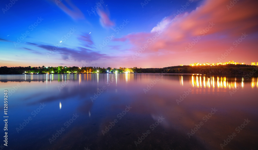 Colorful night landscape on the lake with blue sky and moving clouds reflected in water. Nature back