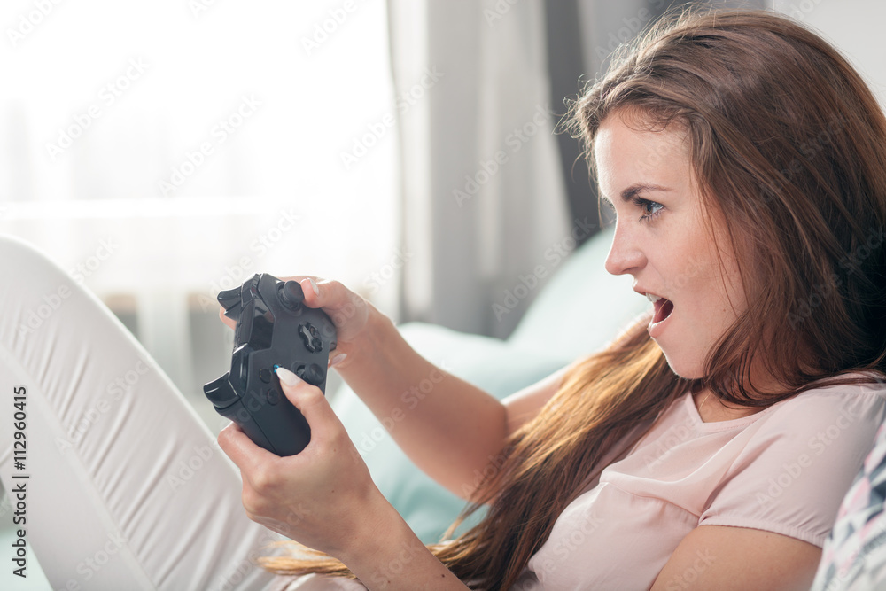 年轻女子坐在家里的沙发上玩电子游戏