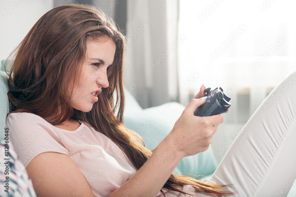 Young woman sitting on couch at home and playing video games