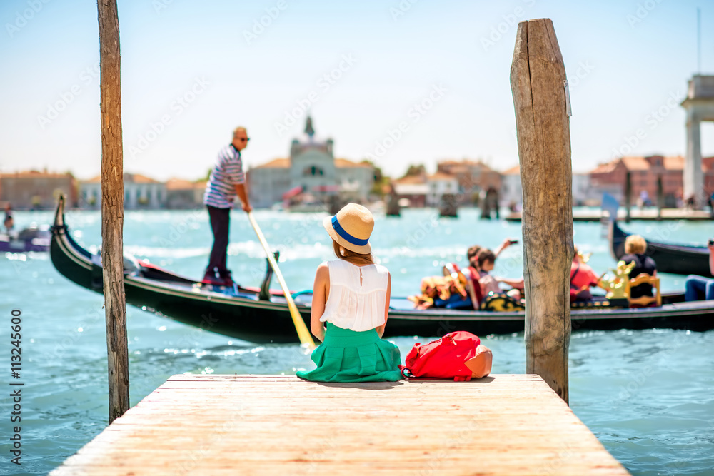 年轻的女旅行者坐在码头上，用贡多拉欣赏威尼斯运河的美景