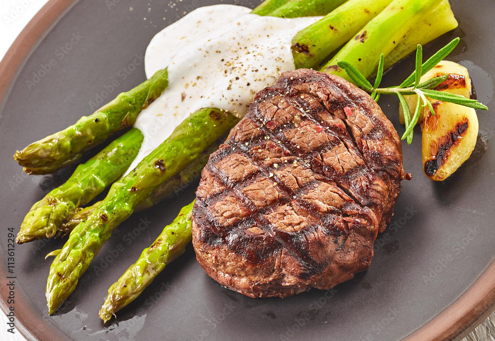 grilled beef steak and asparagus on dark plate
