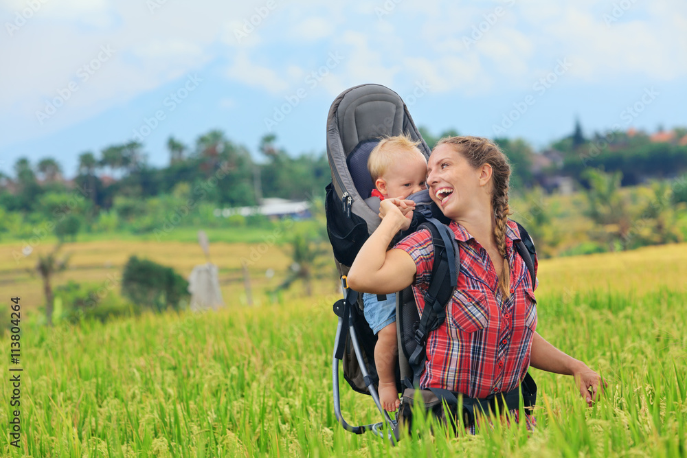 大自然漫步在绿色的稻田里。快乐的母亲背着小旅行者。巴