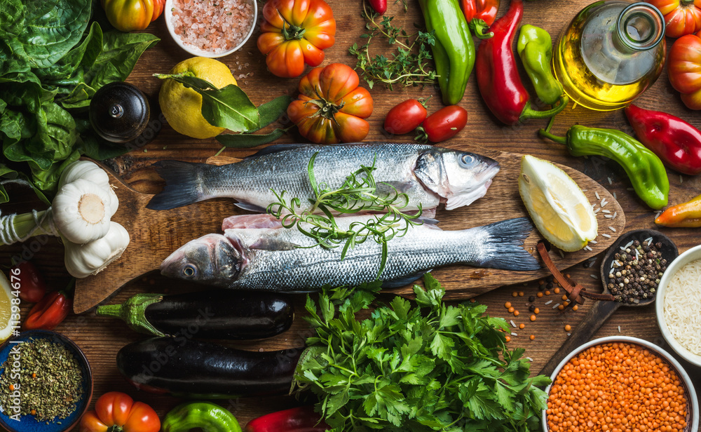 生的未煮熟的鲈鱼，配上蔬菜、谷物、香草和香料，放在乡村的案板上