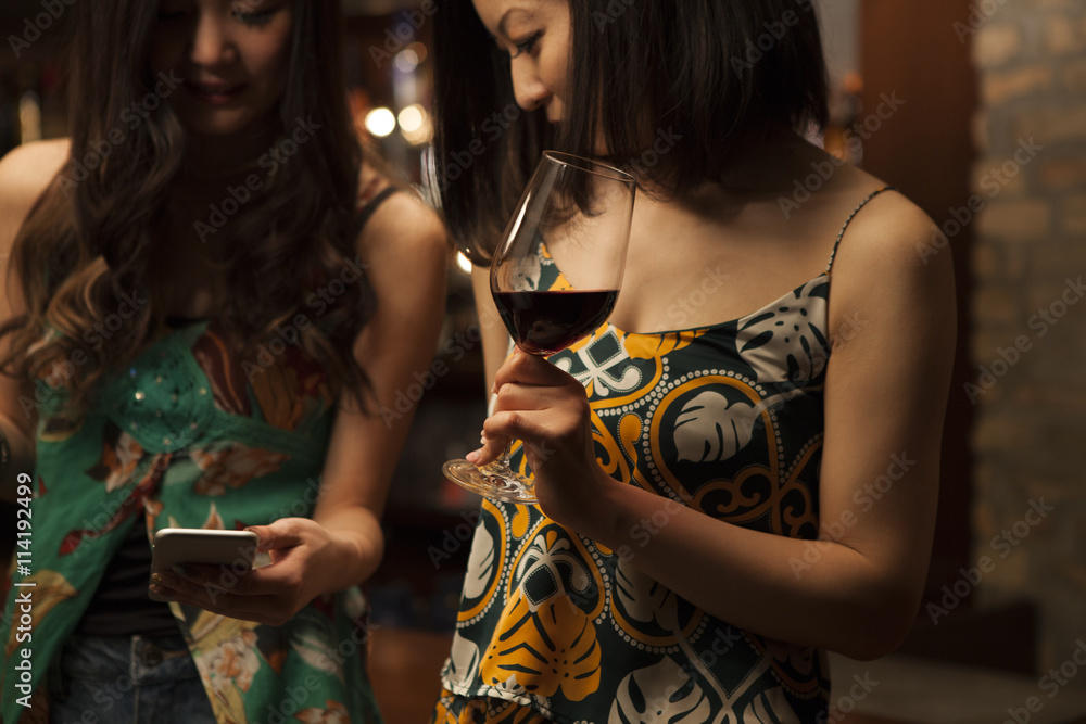 年轻女性在酒吧里拿着一杯葡萄酒看着智能手机